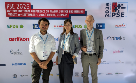 Ein Bild von Dr. Nelson Filipe Lopes Dias, Julia Urbanczyk und Finn Rümenapf (von links nach rechts) vor dem Sponsoren-Hintergrund der PSE2026